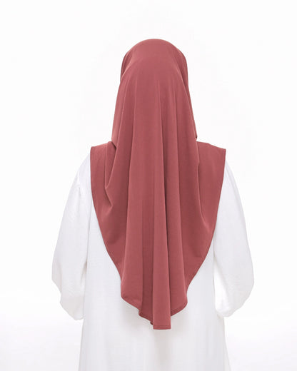 Woman wearing a dusty rose hijab with 'Safiya Sarung Moscrepe' branding.